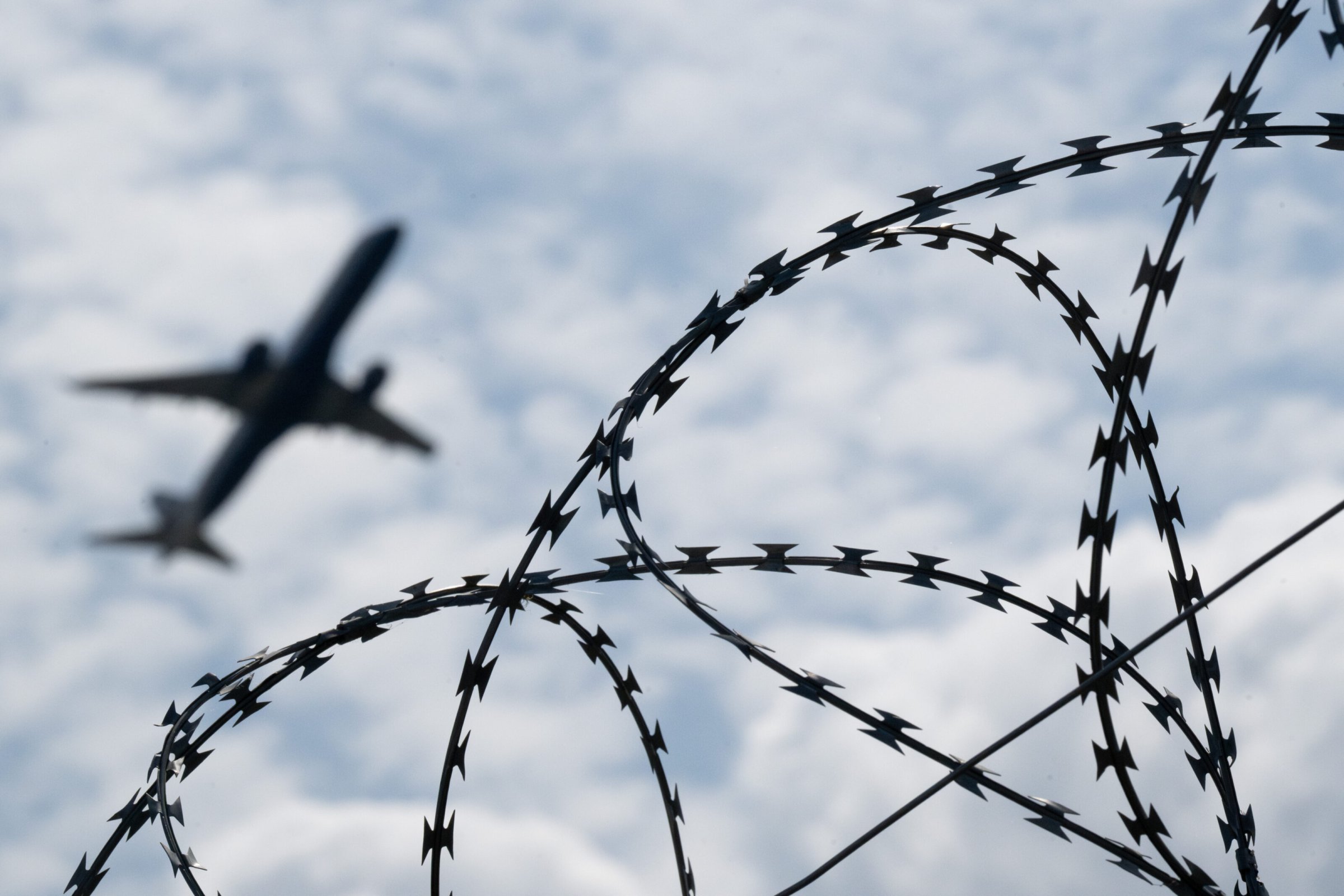 Ein Flugzeug hebt am Flughafen BER hinter einem Zaun mit Natodraht ab.