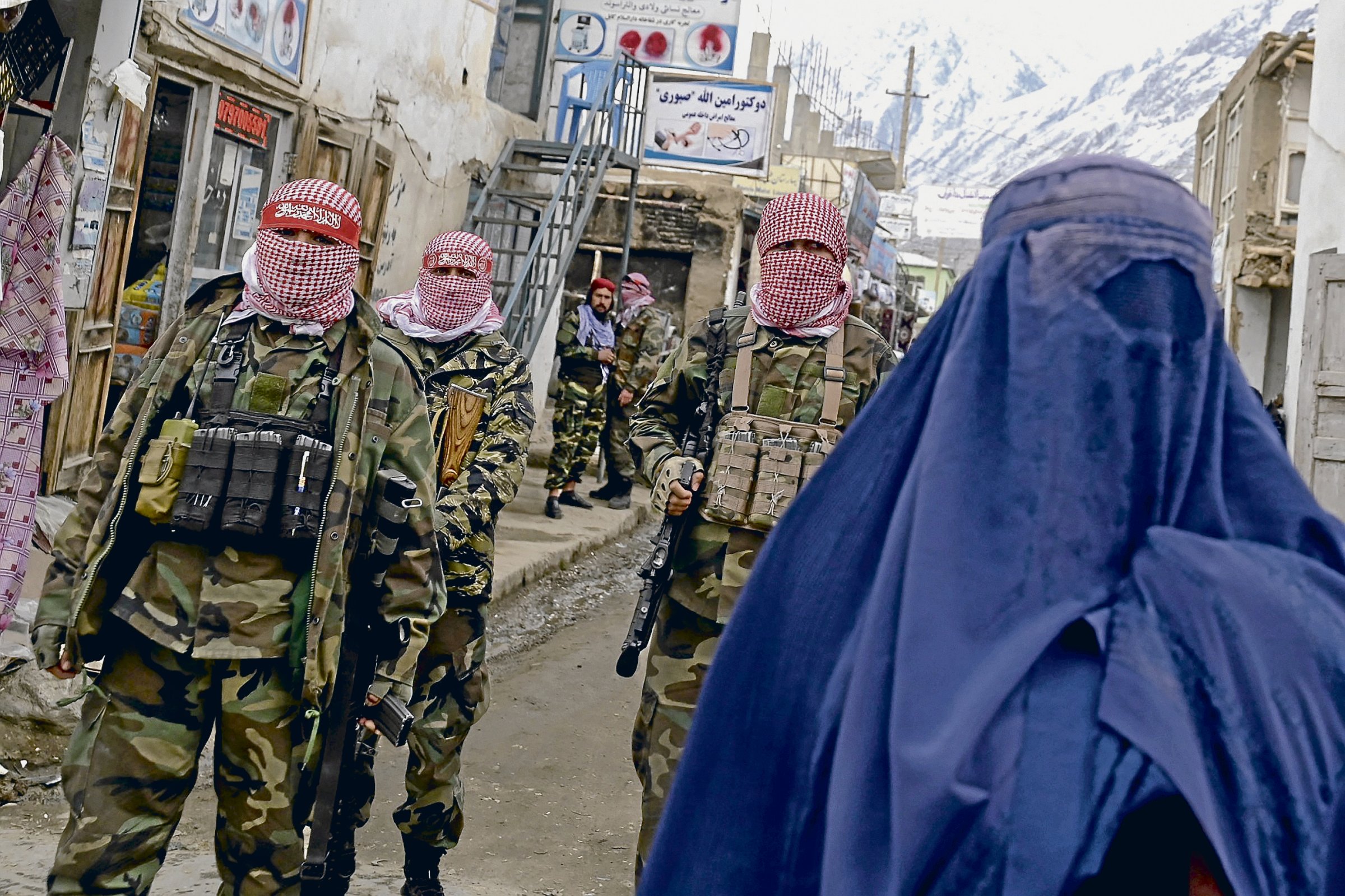 Taliban-Sicherheitskräfte stehen Wache, während eine afghanische Frau in Burka auf einem Markt im Bezirk Baharak in der Provinz Badakhschan eine Straße entlangläuft.