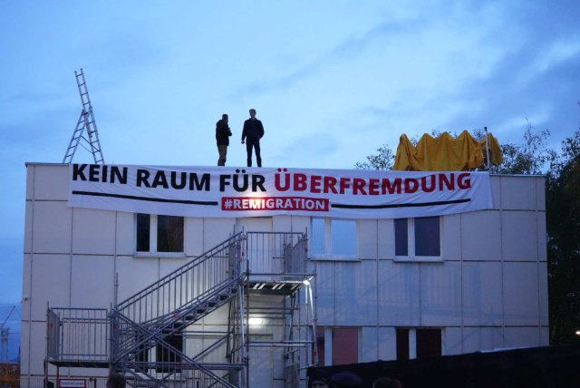 Zwei Rechtsextreme auf dem Dach einer geplanten Asylunterkunft. Die Linke-Gruppe fragt Zahlen zu diesen Taten regelmäßig ab.