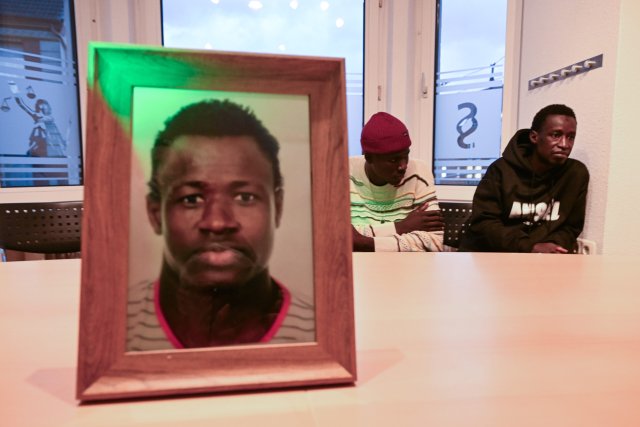 Sidy und Lassana Dramé sitzen in den Räumen ihrer Rechtsanwältin hinter einem Foto ihres von Polizeischüssen getöteten Bruders Mouhamed Dramé.