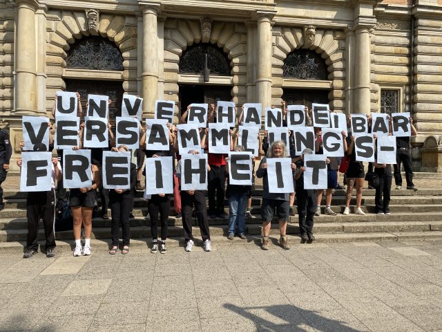 Unterstützer*innen halten vor dem Gerichtsgebäude am Dienstag eine eindeutige Buchstabenkombination in die Höhe.