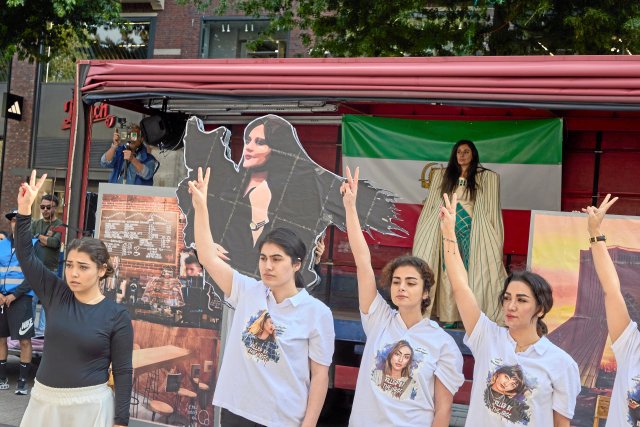 Teilnehmerinnen einer Demonstration Zum Jahrestag der Ermordung von Jina Mahsa Amini performen auf der Mönckebergstraße in Hamburg vor einem Konterfei der Ermordeten.